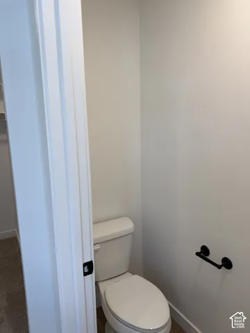 White commode with a matte black toilet paper holder, light-colored walls, and wood-finish flooring