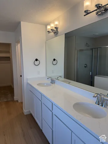 Dual vanity with integrated sinks, white cabinetry, chrome fixtures, and wood-finish flooring