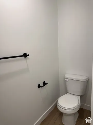 White toilet with a round bowl, matte black towel bar, and wood-finish flooring