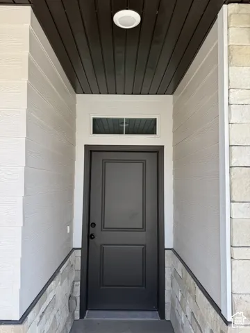 Recessed entry with horizontal plank ceiling, light-toned siding, and a stone veneer base