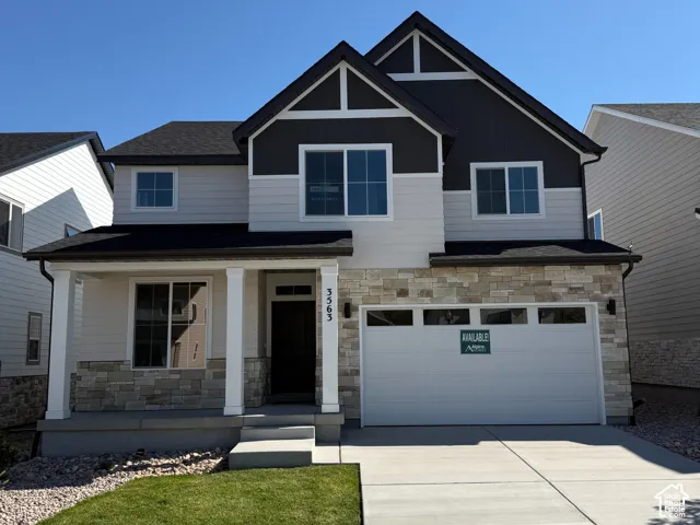 Contemporary architectural styling with dark siding accents, stone detailing on the facade, a covered front porch, an attached garage, and a concrete driveway