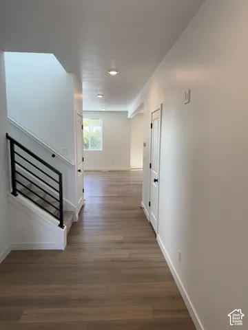 Wood-finish flooring, recessed lighting, white walls, white trim, and a staircase with a black metal railing