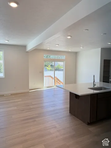 Recessed lighting throughout, wood-finish flooring, sliding glass door leading to an outdoor deck, kitchen island with an undermount sink, and white countertops