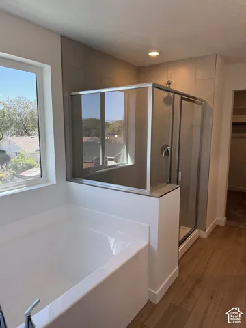 Soaking tub with chrome fixtures, glass-enclosed shower, wall-mounted shower head, and wood-finish flooring