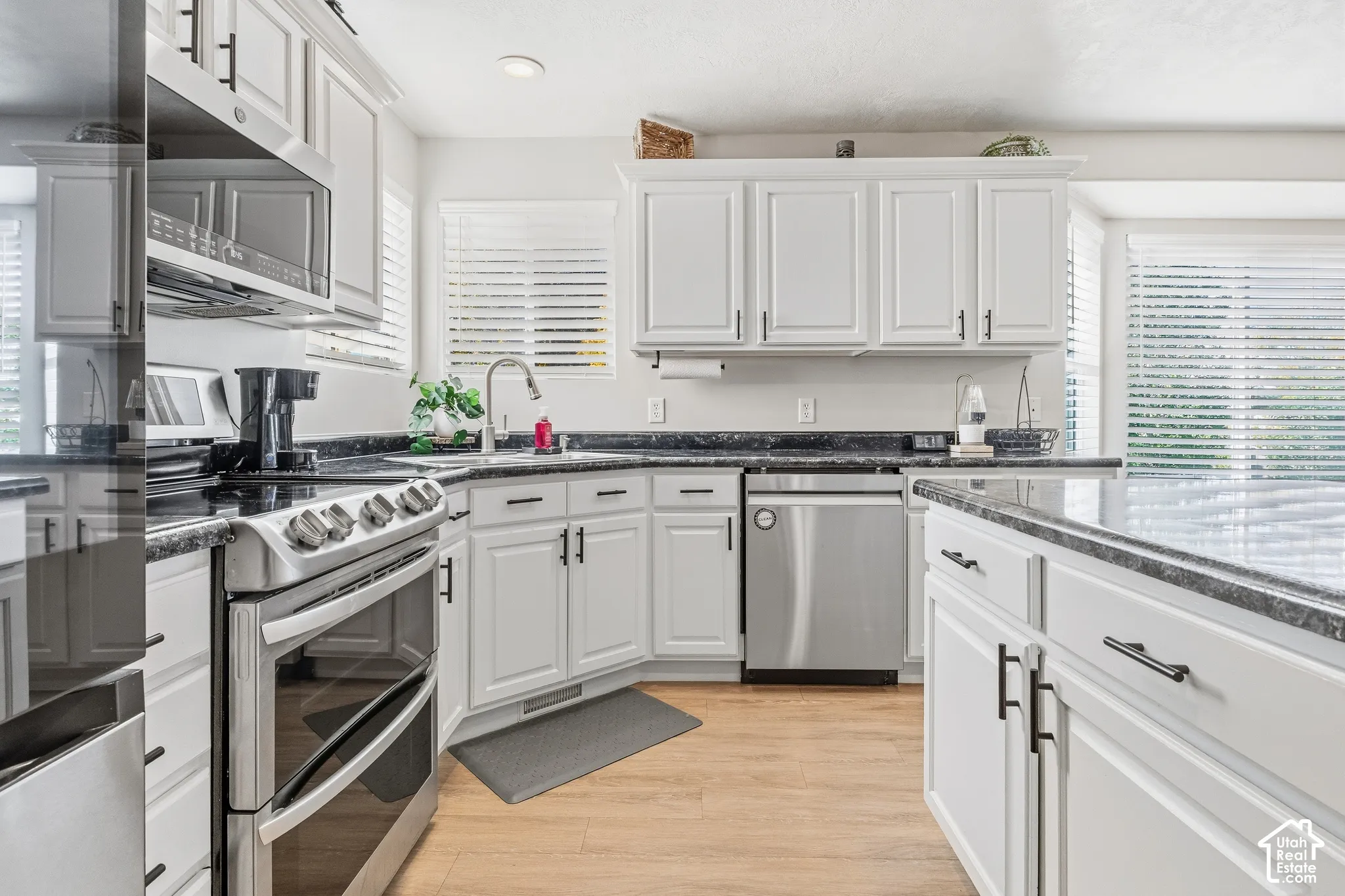 Kitchen featuring white cabinetry, black countertops, stainless steel appliances, and wood-finish flooring
