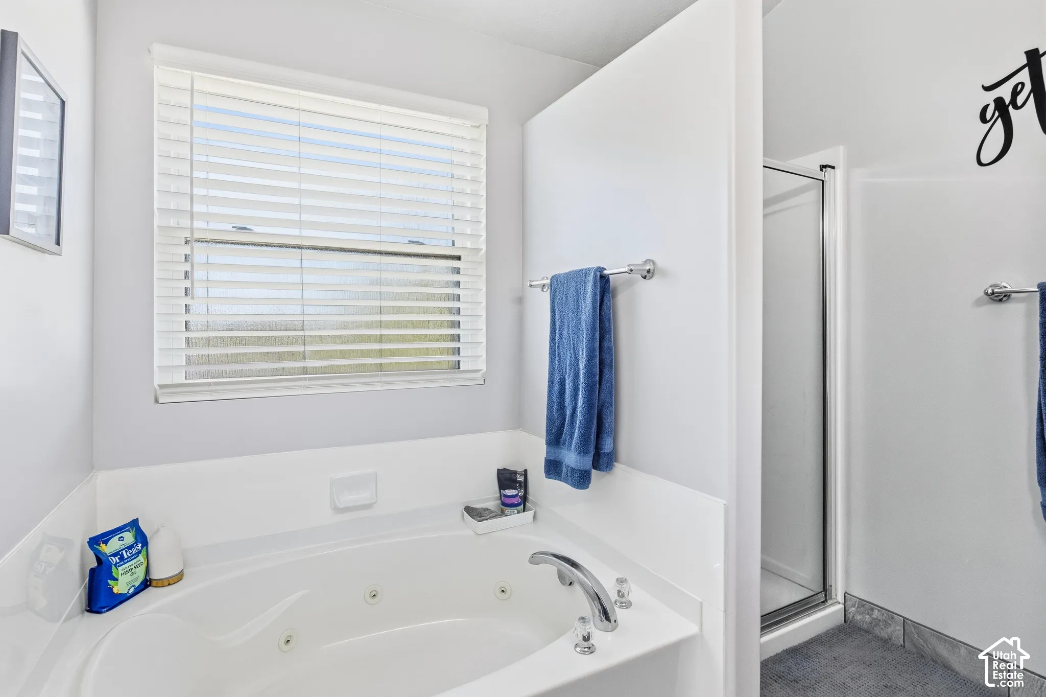 Soaking tub with chrome fixtures, an adjacent shower enclosure, and a window with blinds