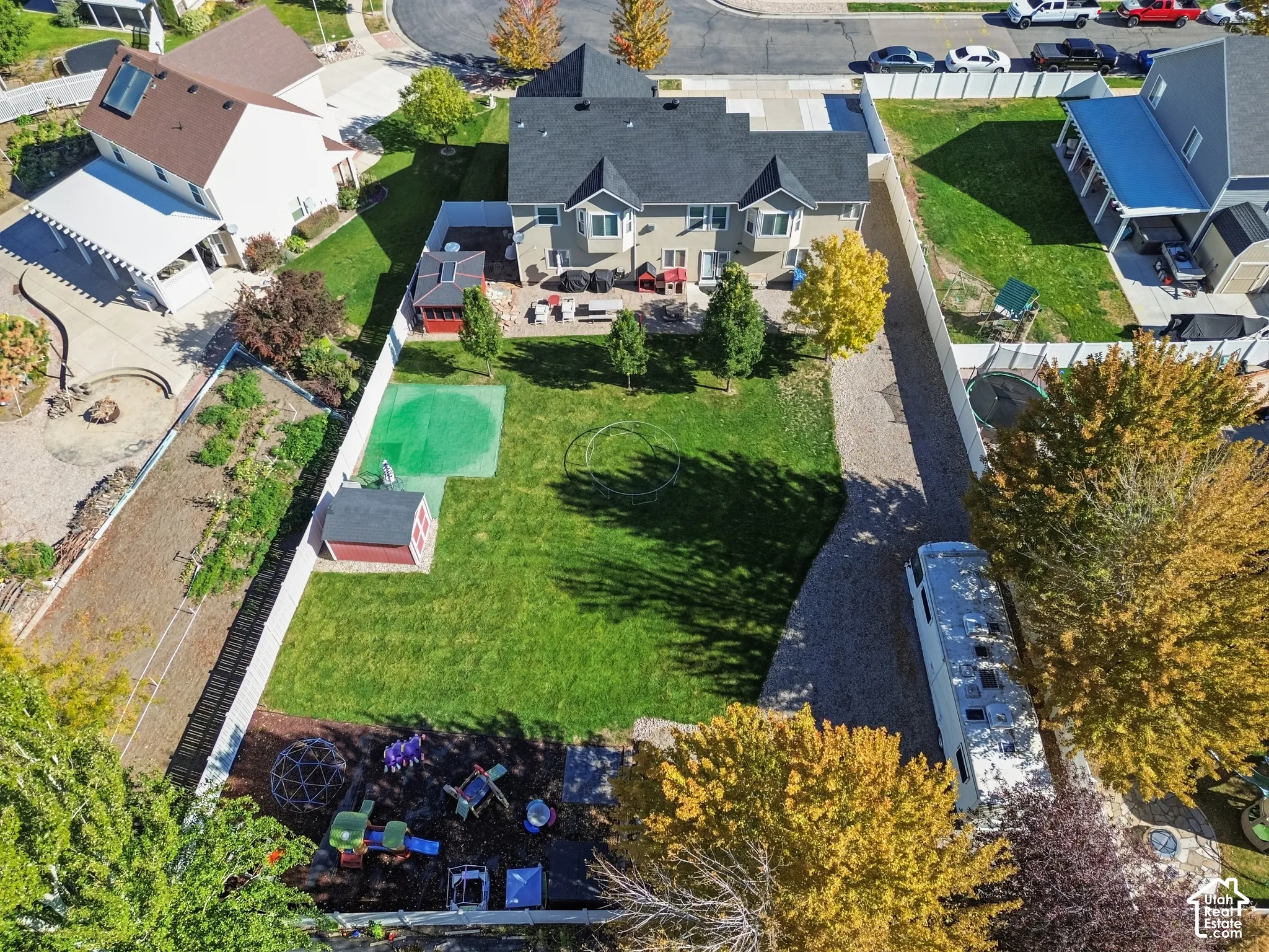 Expansive fenced backyard featuring a grassy lawn, mature trees, a storage shed, and a dedicated gravel area