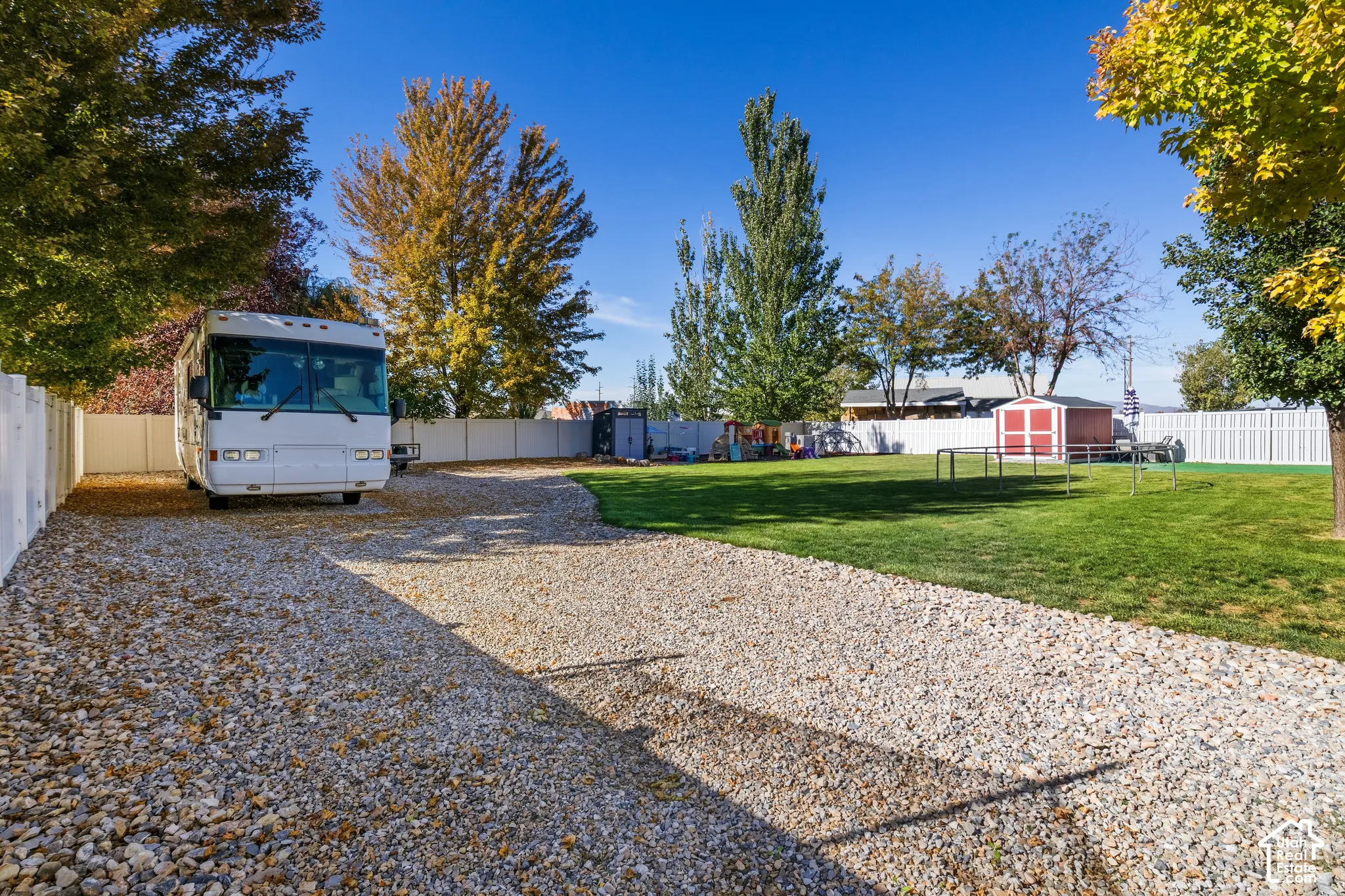 Expansive gravel driveway with a white privacy fence and a manicured lawn