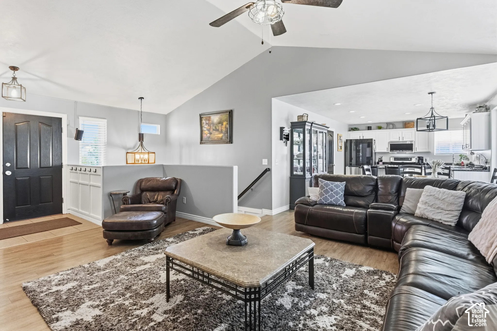 Open-concept living area with wood-finish flooring, vaulted ceilings, and a modern ceiling fan
