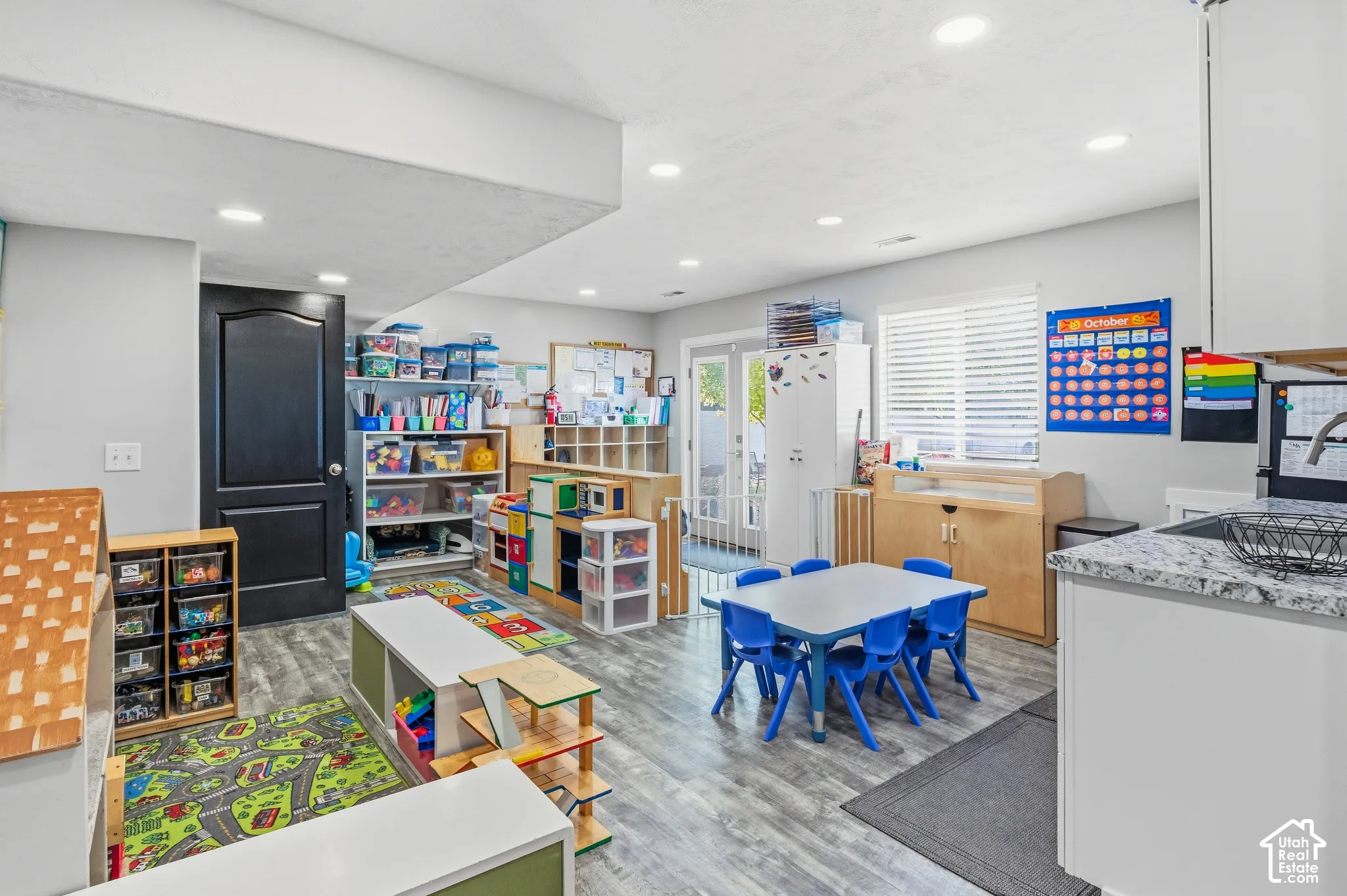 Recessed lighting, wood-finish flooring, white cabinets, light-toned countertop, and a window with blinds