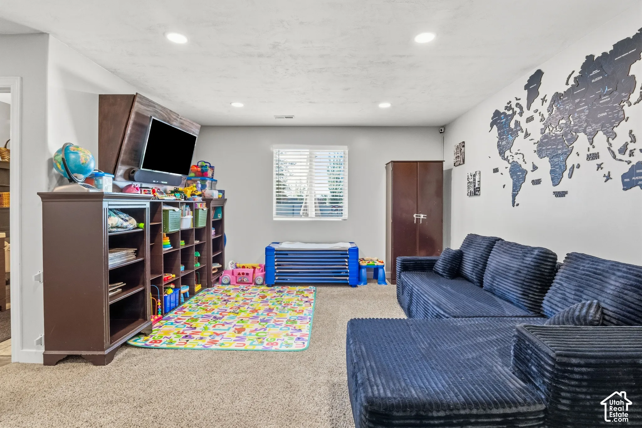 Recessed lighting, wood-finish shelving unit, window with blinds, carpeted flooring, and a built-in wall map feature