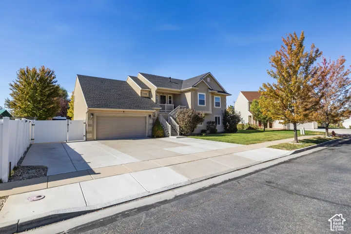 Two-story stucco exterior with an attached garage, asphalt shingle roof, concrete driveway, and white privacy fencing