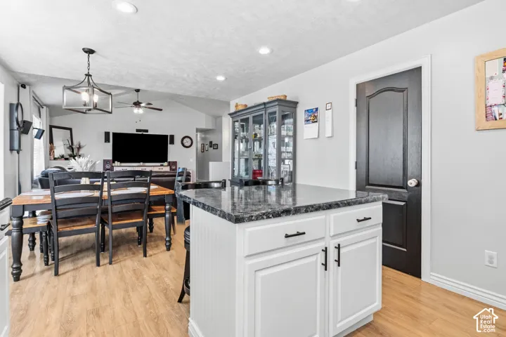 Kitchen island with white cabinetry, dark countertop, and black hardware
