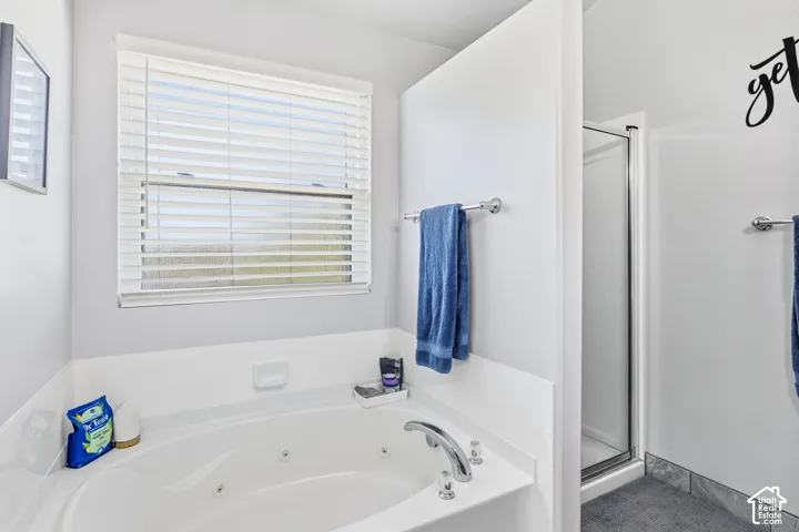 Soaking tub with chrome fixtures, an adjacent shower enclosure, and a window with blinds