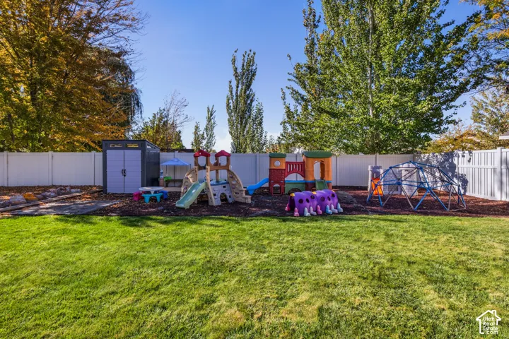 Expansive backyard featuring a manicured lawn, white privacy fencing, and a built-in storage shed