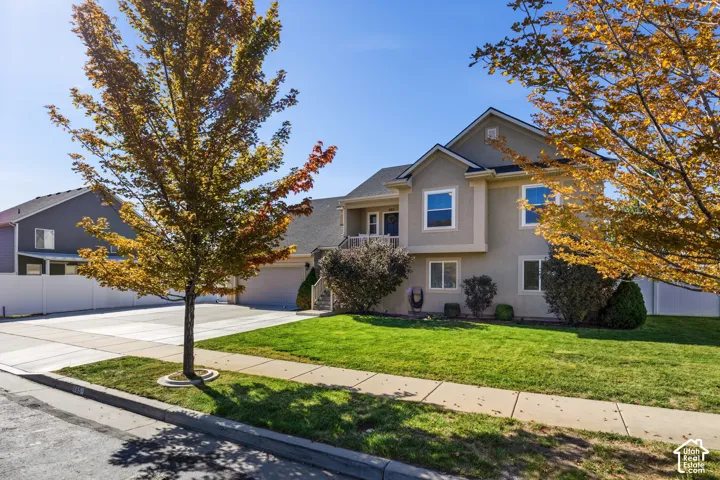 Stucco exterior with multiple windows, an attached garage, a concrete driveway, and a front lawn with mature trees