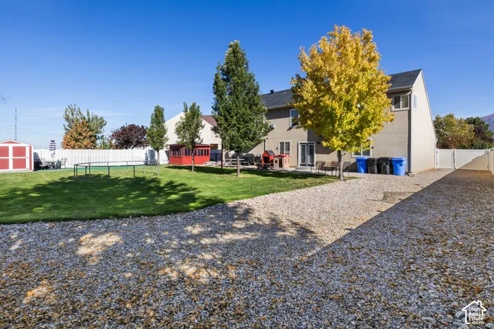 Expansive gravel driveway leading to a private backyard with a white vinyl fence and mature trees