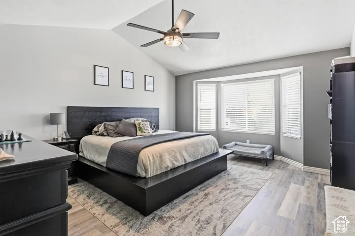 Vaulted ceiling with a ceiling fan, bay window with blinds, wood-finish flooring, and black bedroom furniture