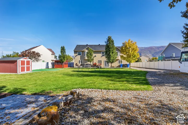 Expansive backyard featuring a manicured lawn, gravel hardscaping, a red storage shed, and a privacy fence