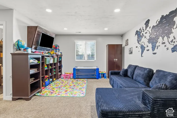 Recessed lighting, wood-finish shelving unit, window with blinds, carpeted flooring, and a built-in wall map feature