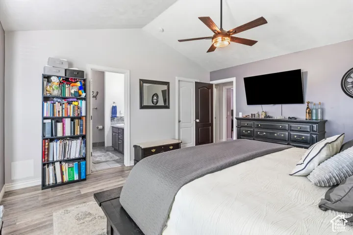 Vaulted ceiling with a ceiling fan, wood-finish flooring, and a private attached bathroom with a vanity and tiled floor