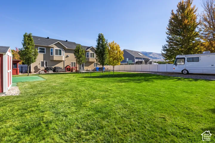 Expansive rear yard featuring a large lawn, mature trees, and a detached storage shed