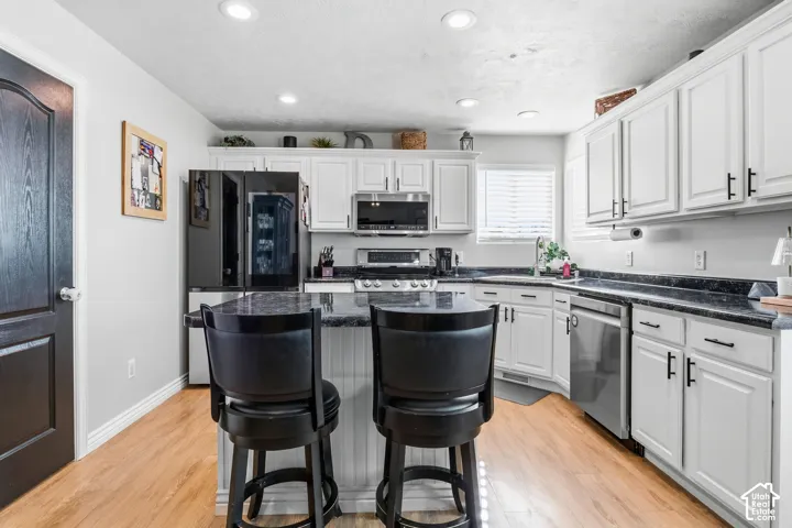 White cabinetry with black hardware, dark stone-finish countertops, stainless steel appliances, wood-finish flooring, and recessed lighting