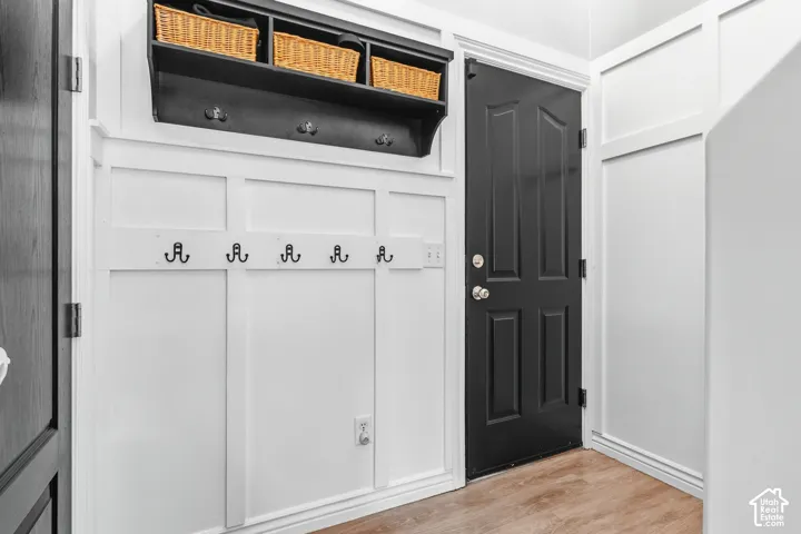 White board-and-batten wall paneling, black paneled door with silver hardware, wood-finish flooring, and a built-in black coat rack with shelf storage