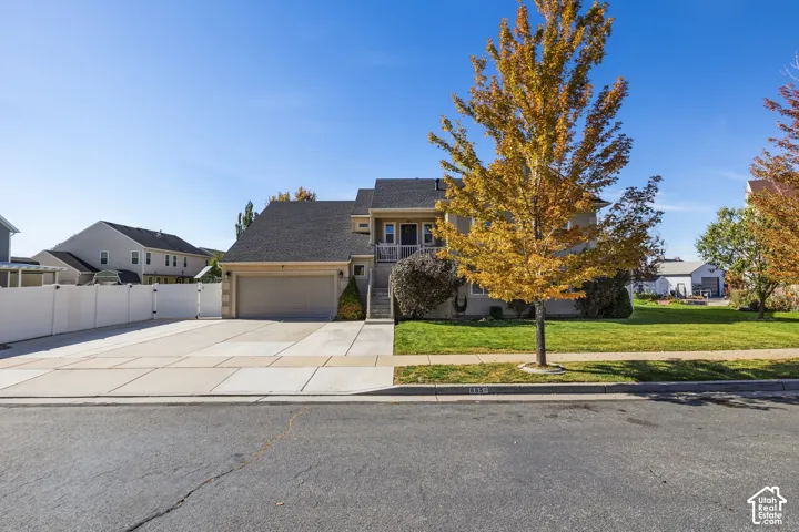 Two-story residence featuring a two-car garage, concrete driveway, and a front lawn with mature trees
