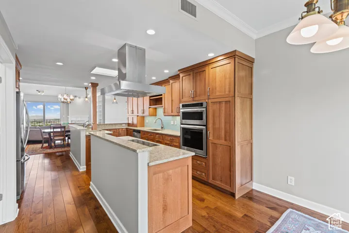 Open-concept kitchen with wood-finish flooring, light wood cabinetry, stainless steel appliances, and a central island with a light-toned countertop
