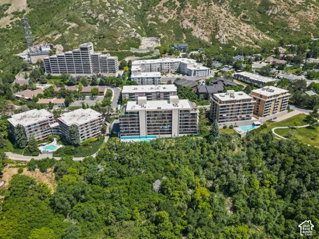 Aerial perspective showcasing multiple residential buildings, surrounded by extensive green foliage and mountainous terrain