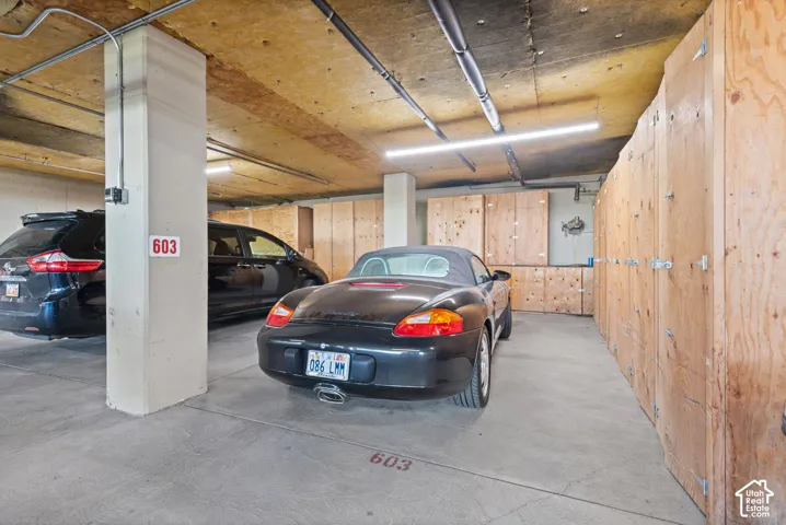 Underground parking space with concrete flooring, exposed ceiling conduit, and fluorescent lighting
