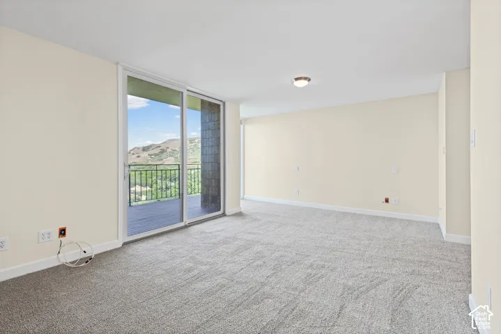 Spacious room with light-colored walls, gray carpeting, and a sliding glass door leading to a balcony