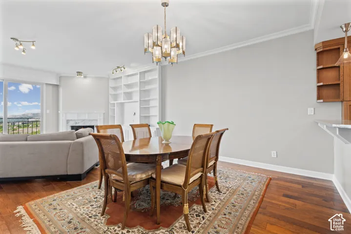 Hardwood flooring, crown molding, built-in shelving, marble fireplace surround, and a contemporary chandelier