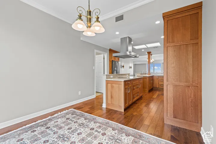 Open-concept kitchen with wood-finish flooring, custom wood cabinetry, and a large stainless steel range hood