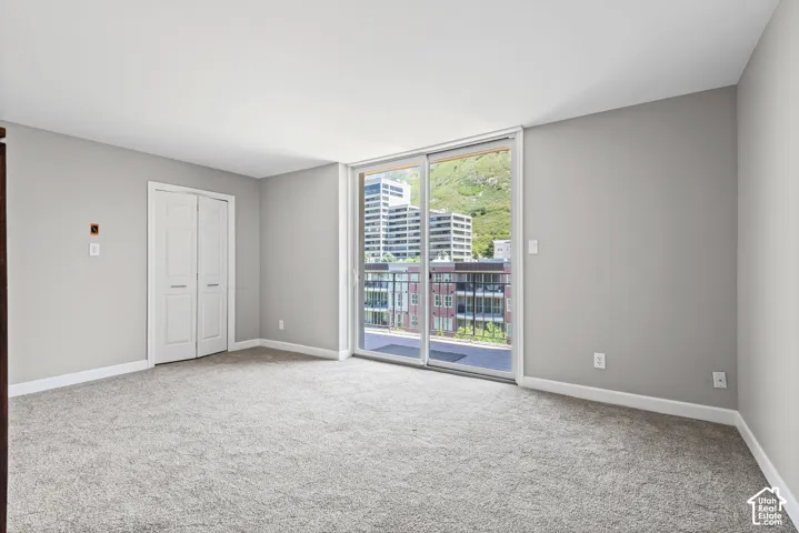 Light gray walls with white trim, gray carpet, white bi-fold closet doors, and sliding glass doors opening to a balcony