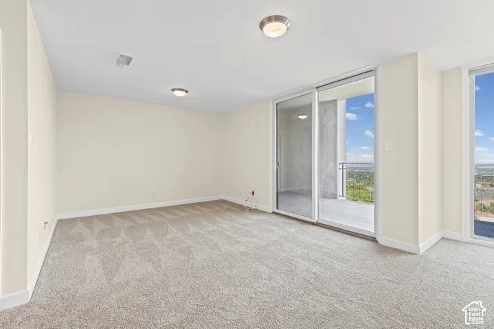 Cream-colored walls with white trim, light-colored carpet flooring, recessed ceiling lighting, and large sliding glass doors leading to an outdoor balcony