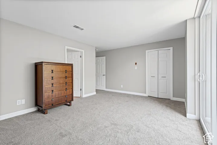Spacious room featuring light gray wall paint, light-colored carpeting, white trim, and a white bi-fold closet door
