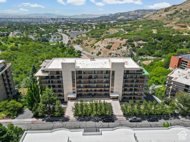 Multi-story building featuring balconies, a paved drive, and surrounding mature trees and foliage