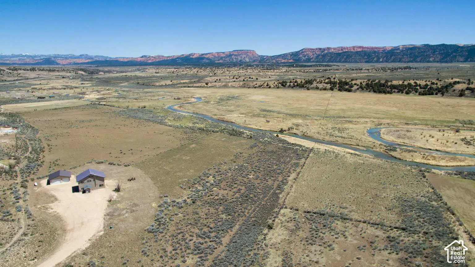 Expansive land featuring a winding river, distant mountain ranges, and a detached structure with a pitched roof