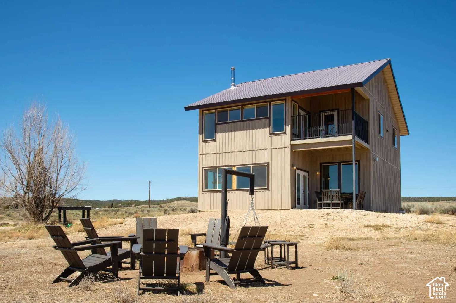 Two-story exterior with a metal roof, an upper-level balcony with metal railing, and a ground-level patio