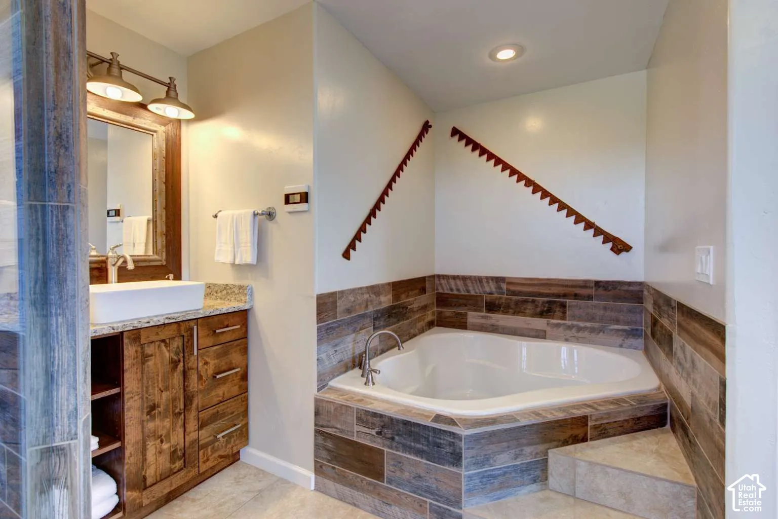 Built-in corner soaking tub with tile surround, wood-finish vanity with countertop, vessel sink, and overhead vanity lighting