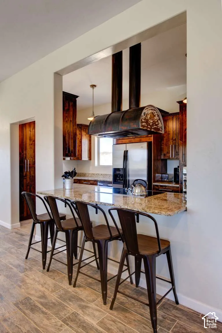 Kitchen pass-through with a stone countertop breakfast bar, wood-finish flooring, and dark wood cabinetry