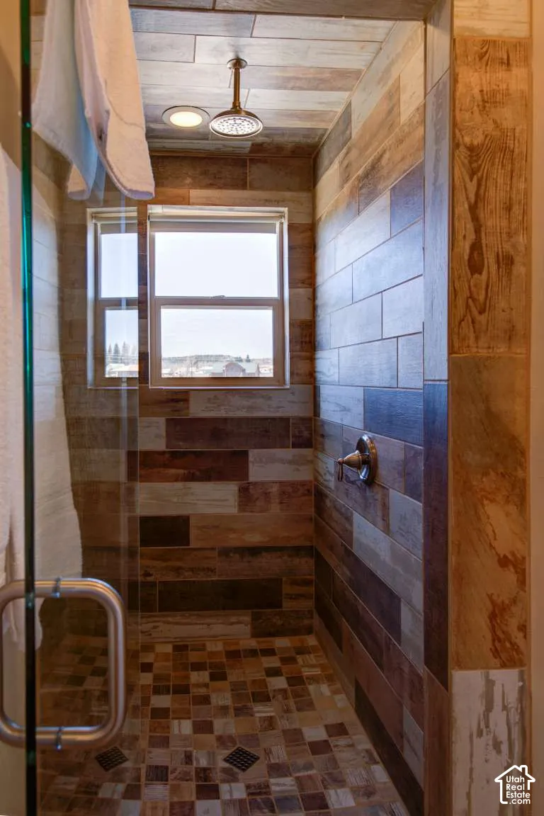 Walk-in shower with varied wood-look wall tiling, mosaic floor tiling, a clear glass enclosure, and a bronze rain showerhead