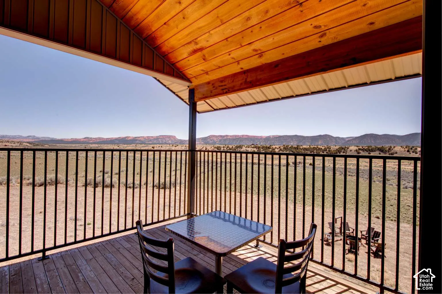 Covered balcony with wood-plank flooring, black metal railing, and wood-paneled ceiling