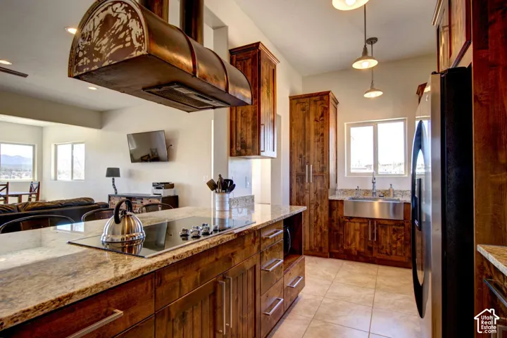 Kitchen featuring wood cabinetry, light-toned granite countertops, stainless steel appliances, and a central island with an integrated cooktop