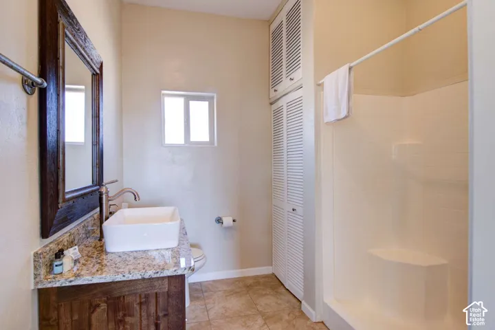 Wood-finish vanity with a vessel sink, stone countertop, and brushed nickel faucet