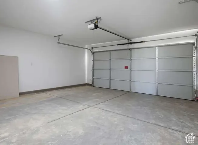 Spacious garage featuring a concrete floor, painted walls, an automatic garage door opener, and a panel-style garage door