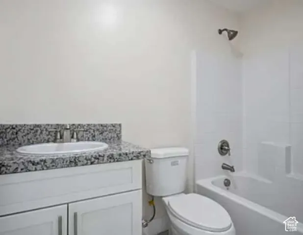 White shaker-style vanity with polished chrome hardware, stone-finish countertop, single-basin sink, and a white toilet