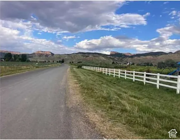 Expansive outdoor area featuring a white perimeter fence, manicured grass, and a paved road